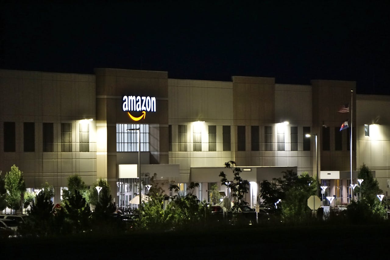 Amazon warehouse building illuminated at night with trees and signage.